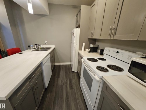 Kitchen featuring gray cabinetry, white countertops, stainless steel sink, wood-finish flooring, and white appliances - 13309 104 Street Nw, Edmonton, AB - Indoor Photo Showing Kitchen With Double Sink