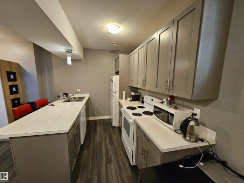 Kitchen featuring wood-finish flooring, gray flat-panel cabinetry, light-toned countertops, and a full suite of white appliances - 13309 104 Street Nw, Edmonton, AB - Indoor Photo Showing Kitchen With Double Sink