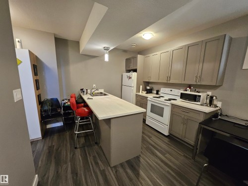 Kitchen area featuring wood-finish flooring, light gray cabinetry, white countertops, and a full suite of white appliances - 13309 104 Street Nw, Edmonton, AB - Indoor Photo Showing Kitchen With Double Sink