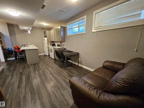Open-concept living area featuring wood-finish flooring, a kitchen island with seating, white appliances, and gray shaker-style cabinetry - 13309 104 Street Nw, Edmonton, AB - Indoor