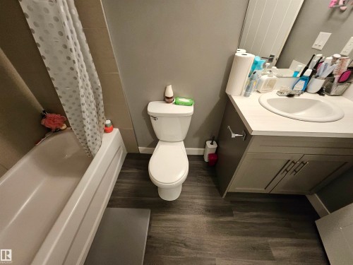 Bathroom featuring wood-finish flooring, a white bathtub, a toilet, and a vanity with an integrated sink and base cabinetry - 13309 104 Street Nw, Edmonton, AB - Indoor Photo Showing Bathroom