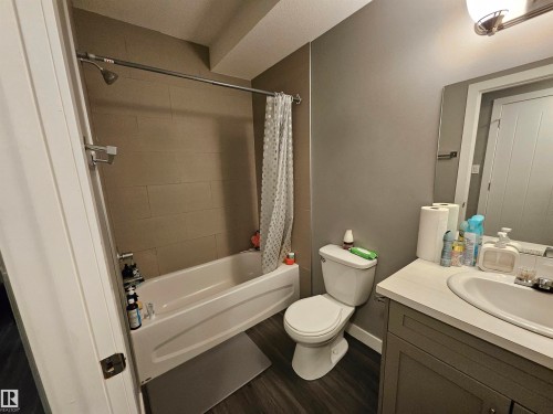 Full bathroom featuring a white bathtub with tile surround, a built-in vanity with a white countertop and integrated sink, a white toilet, and wood-finish flooring - 13309 104 Street Nw, Edmonton, AB - Indoor Photo Showing Bathroom
