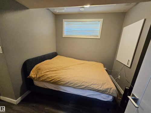 Bedroom featuring wood-finish flooring, a white window frame with horizontal blinds, and a built-in wall cabinet with silver-tone hardware - 13309 104 Street Nw, Edmonton, AB - Indoor Photo Showing Bedroom