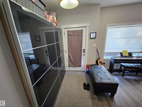 Modern hallway featuring wood-finish flooring, a white trim window with blinds, and a built-in closet with reflective paneled doors - 13309 104 Street Nw, Edmonton, AB - Indoor Photo Showing Other Room