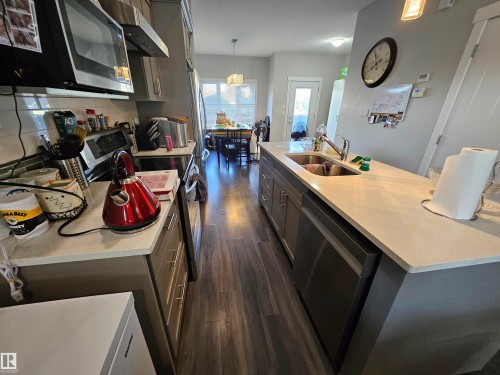 Modern kitchen featuring wood-finish flooring, light grey cabinetry, stainless steel appliances, a tile backsplash, and light-toned countertops - 13309 104 Street Nw, Edmonton, AB - Indoor Photo Showing Kitchen With Double Sink