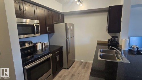 Kitchen featuring dark wood cabinetry, stainless steel appliances, dark countertops, a double basin sink, and wood-finish flooring - 1510 Watt Drive Southwest, Edmonton, AB - Indoor Photo Showing Kitchen With Stainless Steel Kitchen With Double Sink