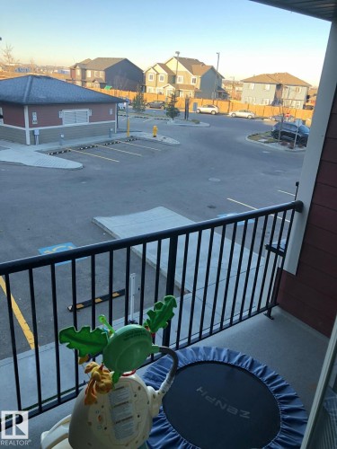 Balcony with black metal railings overlooking a paved parking area and a red and beige building with a dark roof - 1510 Watt Drive Southwest, Edmonton, AB - Outdoor