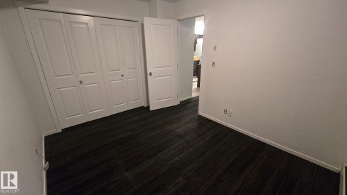 Room featuring dark patterned carpet flooring, white walls, white baseboards, and white bi-fold closet doors - 1510 Watt Drive Southwest, Edmonton, AB - Indoor Photo Showing Other Room