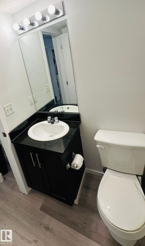 Bathroom featuring a white toilet, black vanity with an integrated sink, dark countertop, and wood-finish flooring - 1510 Watt Drive Southwest, Edmonton, AB - Indoor Photo Showing Bathroom