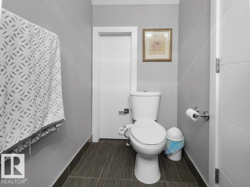 Neutral-toned powder room featuring a white toilet with an attached bidet, dark wood-finish tile flooring, and light gray wall paint - 7909 105 Avenue Nw, Edmonton, AB - Indoor Photo Showing Bathroom
