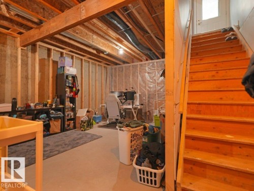 Unfinished basement area featuring exposed wood framing, concrete flooring, and an exposed wood staircase leading to a white door - 7909 105 Avenue Nw, Edmonton, AB - Indoor Photo Showing Basement
