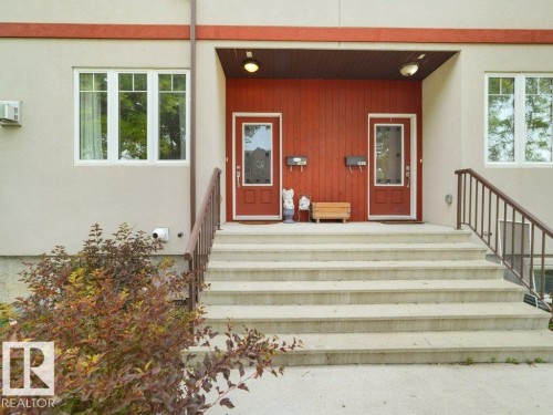 Exterior featuring a dual-entry design with red paneled doors, white-trimmed windows, a light-toned stucco facade, and a multi-level concrete staircase with railings - 7909 105 Avenue Nw, Edmonton, AB -  With Exterior