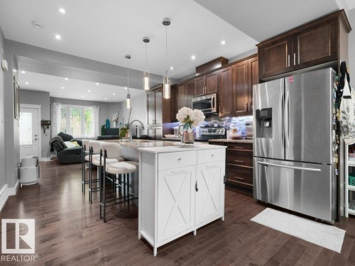 Open-concept kitchen featuring dark wood-finish flooring, recessed lighting, a kitchen island with pendant lights, dark wood cabinetry, and stainless steel appliances - 7909 105 Avenue Nw, Edmonton, AB - Indoor Photo Showing Kitchen With Upgraded Kitchen