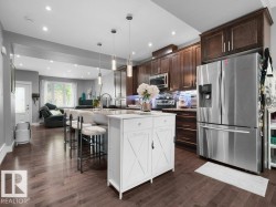 Open-concept kitchen featuring dark wood-finish flooring, recessed lighting, a kitchen island with pendant lights, dark wood cabinetry, and stainless steel appliances - 