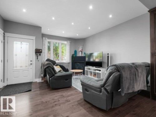 Living area featuring wood-finish flooring, recessed lighting, a white framed window with decorative curtains, and a white entry door with frosted glass panels - 7909 105 Avenue Nw, Edmonton, AB - Indoor