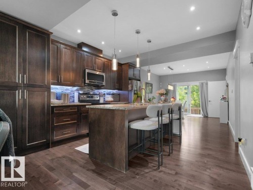 Open-concept kitchen featuring dark wood cabinetry, stainless steel appliances, a center island with bar seating, pendant lighting, and wood-finish flooring extending into the living area - 7909 105 Avenue Nw, Edmonton, AB - Indoor Photo Showing Kitchen With Upgraded Kitchen