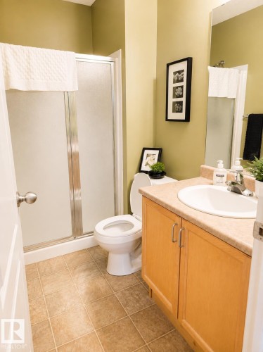 Bathroom featuring a shower with a frosted glass enclosure, a vanity with a light wood-finish cabinet, a single basin sink, a light-toned countertop, and square floor tiles - #202 16715 100 Av Nw, Edmonton, AB - Indoor Photo Showing Bathroom