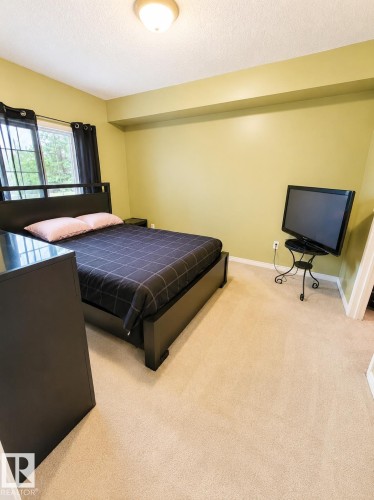 Carpeted room with a ceiling-mounted light fixture, featuring a window with dark drapes - #202 16715 100 Av Nw, Edmonton, AB - Indoor