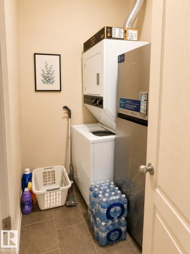 Dedicated laundry closet featuring a stacked washer and dryer, tile flooring, and a solid core interior door - #202 16715 100 Av Nw, Edmonton, AB - Indoor Photo Showing Laundry Room