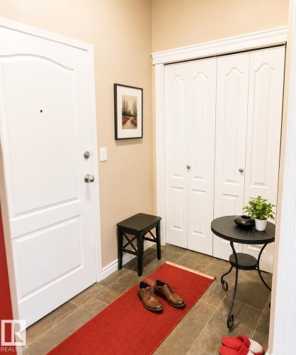 Entryway featuring a paneled door with brushed nickel hardware, tan wall paint, and brown tile flooring - #202 16715 100 Av Nw, Edmonton, AB - Indoor Photo Showing Other Room