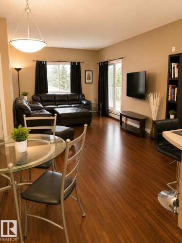 Open-concept living area with wood-finish flooring, a contemporary ceiling light fixture, and a sliding glass door providing outdoor access - #202 16715 100 Av Nw, Edmonton, AB - Indoor
