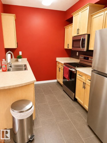 Galley kitchen featuring light wood cabinetry, light-toned countertops, and stainless-steel appliances - #202 16715 100 Av Nw, Edmonton, AB - Indoor Photo Showing Kitchen With Double Sink