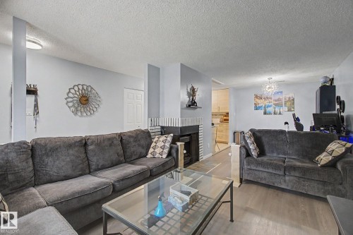 Spacious living area featuring wood-finish flooring, a fireplace with a white brick surround, and a ceiling-mounted light fixture - #39 3111 142 Av Nw, Edmonton, AB - Indoor Photo Showing Living Room