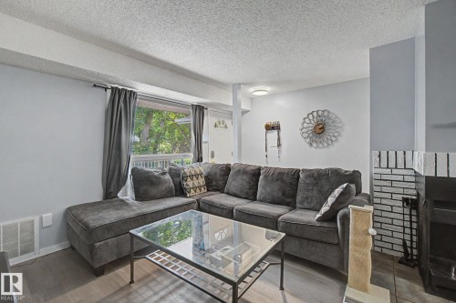 Bright living area featuring light gray walls, wood-finish flooring, and a large window with outdoor greenery - #39 3111 142 Av Nw, Edmonton, AB - Indoor Photo Showing Living Room