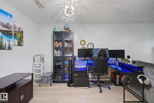 Versatile room featuring light wood-finish flooring, a contemporary ceiling light fixture, and a built-in glass-front storage cabinet - #39 3111 142 Av Nw, Edmonton, AB - Indoor Photo Showing Office