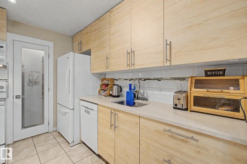 Kitchen with light wood-finish cabinetry, white appliances, and a solid surface countertop - #39 3111 142 Av Nw, Edmonton, AB - Indoor Photo Showing Kitchen