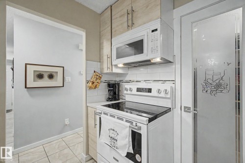 Kitchen featuring white appliances, a white tile backsplash, light wood-finish cabinetry, a built-in microwave, and an adjacent frosted glass pantry door - #39 3111 142 Av Nw, Edmonton, AB - Indoor Photo Showing Kitchen