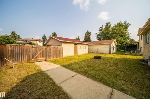 Expansive backyard featuring a manicured lawn, a detached stucco garage with a red roof, a separate storage shed, and a privacy fence with a gate - 1719 37 Street Nw, Edmonton, AB - Outdoor