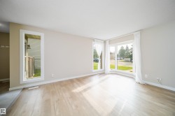 Bright living space featuring a bay window, wood-finish flooring, neutral wall paint, and white trim - 