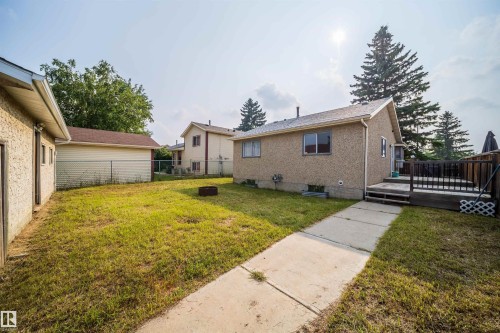 Expansive backyard featuring a concrete pathway, a wooden deck with railing, and mature evergreen trees - 1719 37 Street Nw, Edmonton, AB - Outdoor With Exterior