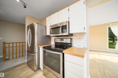 Kitchen featuring stainless steel appliances, white cabinetry, wood-finish countertops, and a white subway tile backsplash - 1719 37 Street Nw, Edmonton, AB - Indoor Photo Showing Kitchen