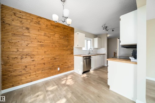Dining area featuring a wood-panel accent wall, overhead chandelier, and light wood-finish flooring - 1719 37 Street Nw, Edmonton, AB - Indoor Photo Showing Kitchen