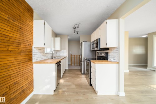 Galley kitchen featuring white cabinetry, stainless steel appliances, wood-finish countertops, subway tile backsplash, and light wood-finish flooring - 1719 37 Street Nw, Edmonton, AB - Indoor Photo Showing Kitchen