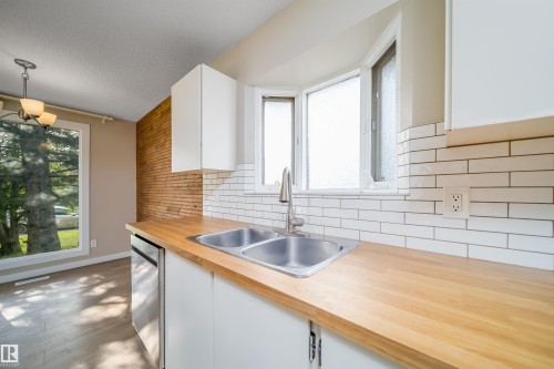 Kitchen featuring a double basin stainless steel sink, wood-finish countertops, white subway tile backsplash, and white cabinetry - 1719 37 Street Nw, Edmonton, AB - Indoor Photo Showing Kitchen With Double Sink