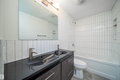 Bathroom featuring a double vanity with dark cabinetry and a black countertop, a soaking tub, and vertical white subway tile in the shower - 1719 37 Street Nw, Edmonton, AB - Indoor Photo Showing Bathroom