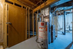 Utility area featuring exposed wood framing, a water heater, and a furnace unit - 