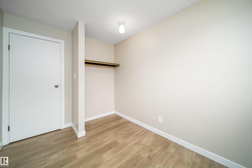 Light-filled room featuring wood-finish flooring, neutral wall tones, and a built-in closet with shelving and hanging rod - 1719 37 Street Nw, Edmonton, AB - Indoor Photo Showing Other Room
