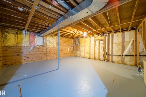 Unfinished basement featuring exposed wood joists, a painted concrete floor, wood paneling on one wall, and framed sections with insulation - 1719 37 Street Nw, Edmonton, AB - Indoor Photo Showing Basement