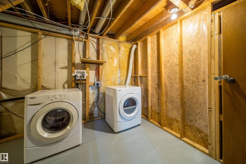 Laundry area featuring a front-loading washing machine, a front-loading dryer, exposed wood joists, a wooden shelf, and a light-colored floor - 1719 37 Street Nw, Edmonton, AB - Indoor Photo Showing Laundry Room