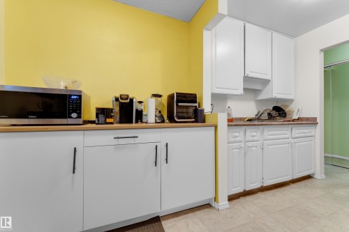 Kitchenette featuring white cabinetry with black hardware, wood-finish countertops, and tile flooring - #104 11445 41 Av Nw, Edmonton, AB - Indoor Photo Showing Kitchen