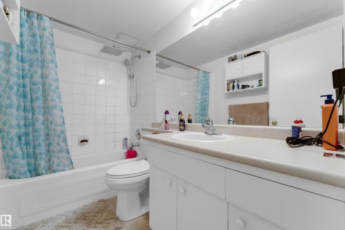 Bathroom featuring a white vanity with an integrated sink, a large wall-mounted mirror, and overhead strip lighting - #104 11445 41 Av Nw, Edmonton, AB - Indoor Photo Showing Bathroom