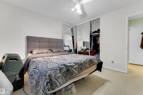 Carpeted room featuring a ceiling fan, light-toned walls, and mirrored closet doors - #104 11445 41 Av Nw, Edmonton, AB - Indoor Photo Showing Bedroom