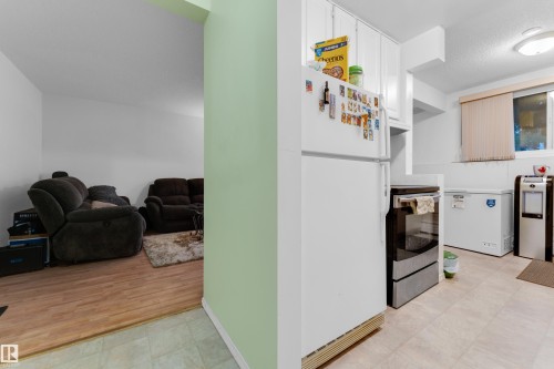 Compact kitchen area with white cabinetry and a white refrigerator, featuring light-toned resilient flooring - #104 11445 41 Av Nw, Edmonton, AB - Indoor
