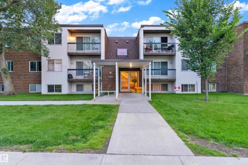 Multi-story residential building featuring brick and vertical siding, individual balconies, a covered entryway, and a concrete pathway - #104 11445 41 Av Nw, Edmonton, AB - Outdoor With Facade