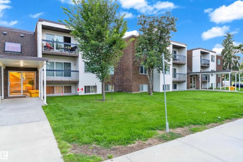 Multi-story building featuring brick and white siding, individual balconies with dark railings, a covered entrance, and a landscaped lawn - #104 11445 41 Av Nw, Edmonton, AB - Outdoor