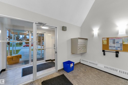Entryway featuring a glass and aluminum door system, wall-mounted mailboxes, a cork bulletin board, wall sconces, and baseboard heating - #104 11445 41 Av Nw, Edmonton, AB - Indoor Photo Showing Other Room